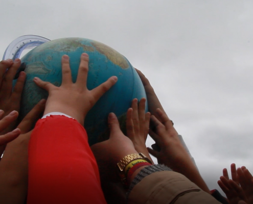 Children's hands raising a globe in the air.